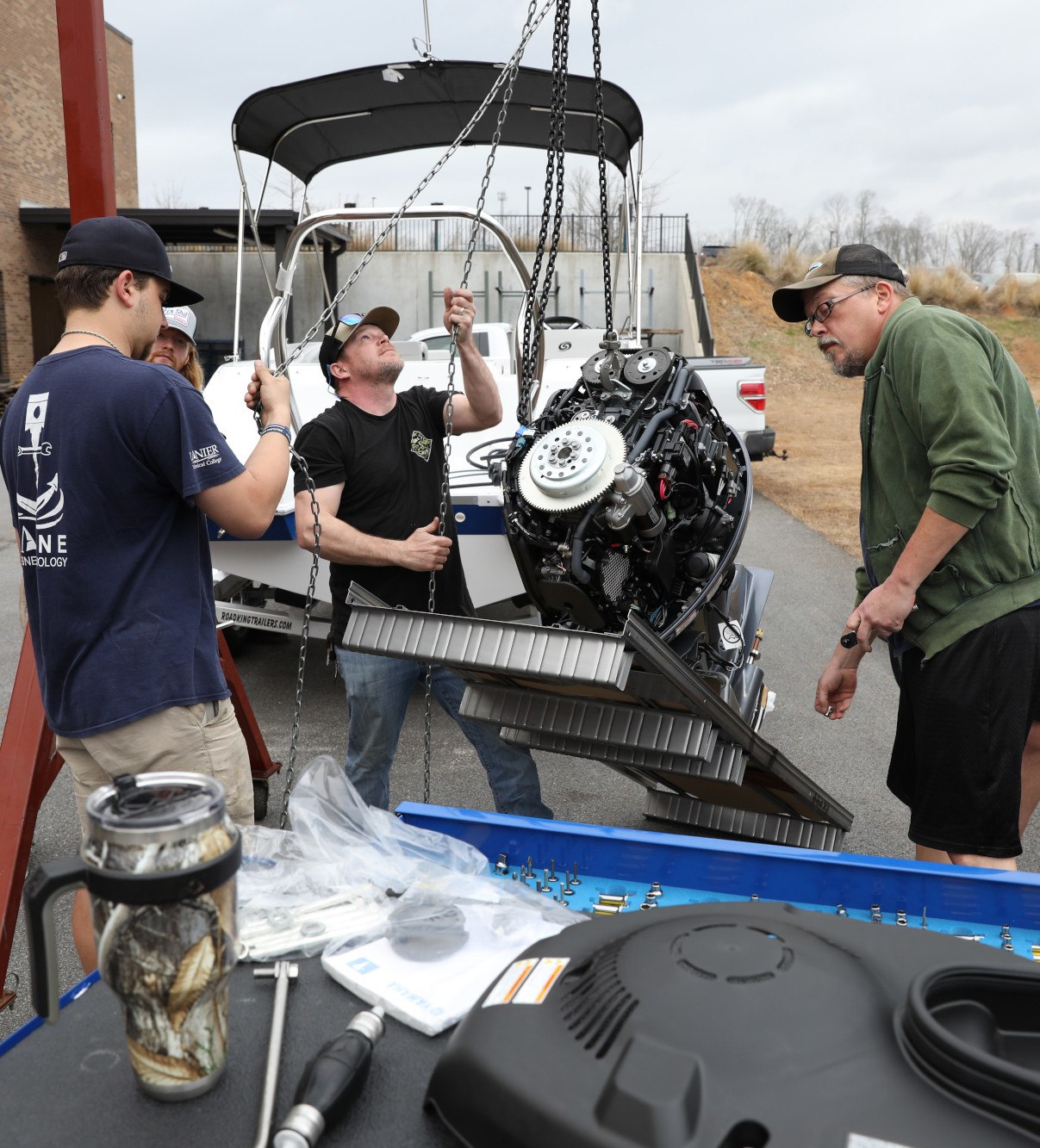 Marine Engine Technology students hoisting up a boats outboard motor