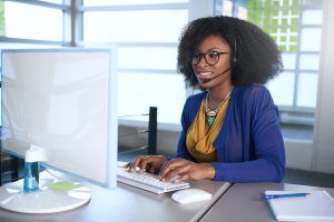 Friendly african american casual call center emplyee working at a desktop computer in a modern white office